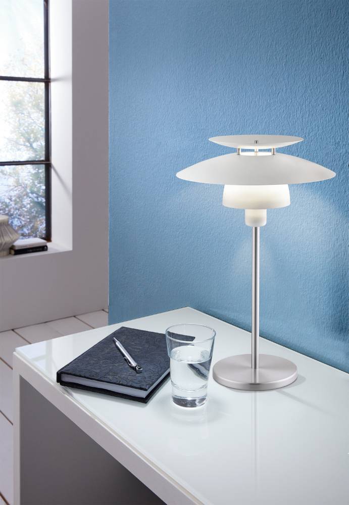 Lampe posée sur un bureau blanc, mur bleu, verre d'eau et carnet noir à proximité.