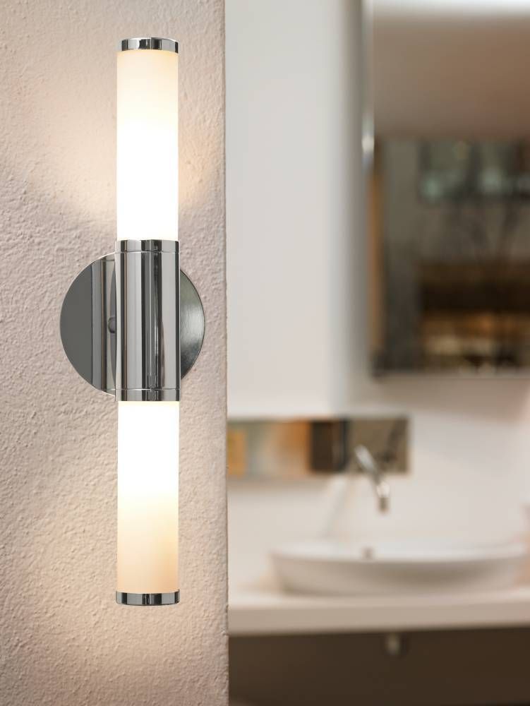 Luminaire installé verticalement sur mur clair, près d'un lavabo et miroir flous