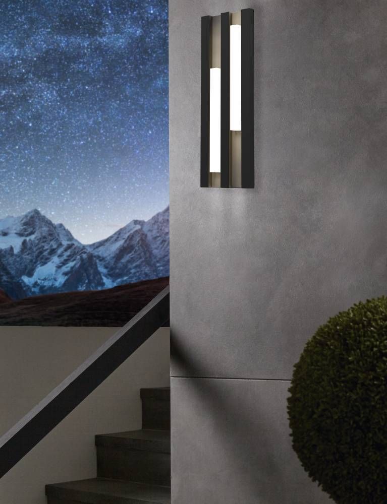 Mise en ambiance nocturne de l’applique allumée sur un mur gris, ciel étoilé et escalier.