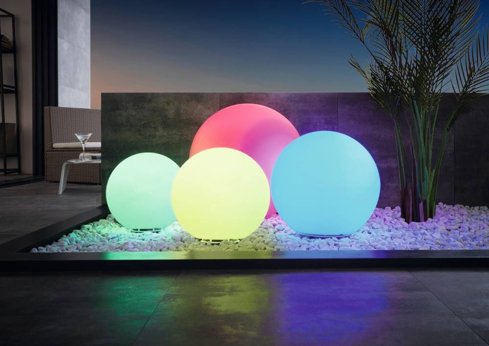 Trois sphères lumineuses colorées installées sur gravier, ambiance extérieure nocturne avec palmier