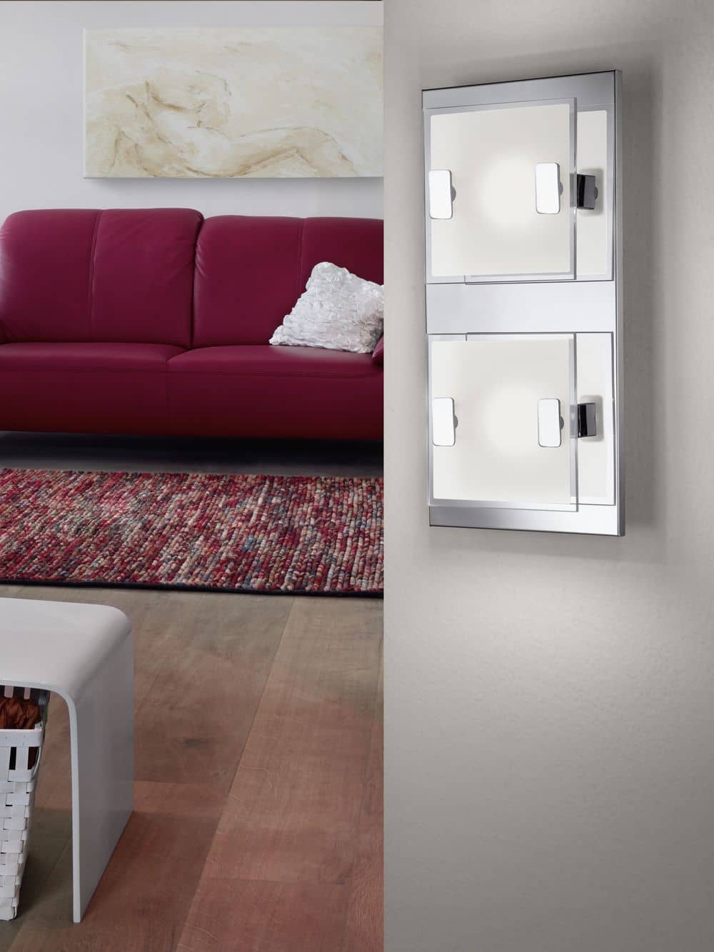 Mise en ambiance : applique murale allumée avec deux carrés lumineux, canapé rouge au fond.