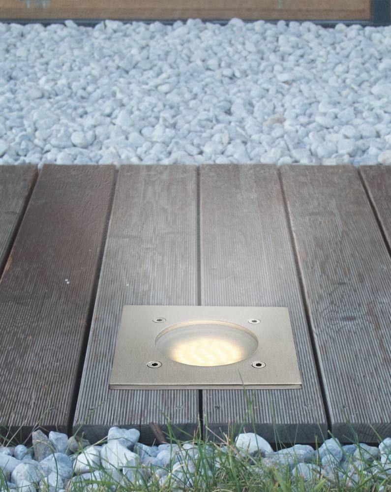 Luminaire encastré installé dans une terrasse en bois, entouré de graviers clairs.