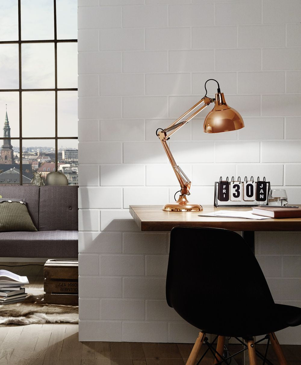 Mise en ambiance : lampe posée sur un bureau en bois devant un mur de briques blanches