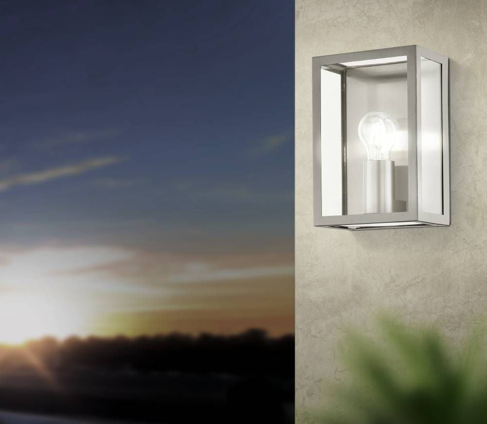 Applique inox allumée fixée sur mur crépit, ciel de crépuscule orangé en arrière-plan