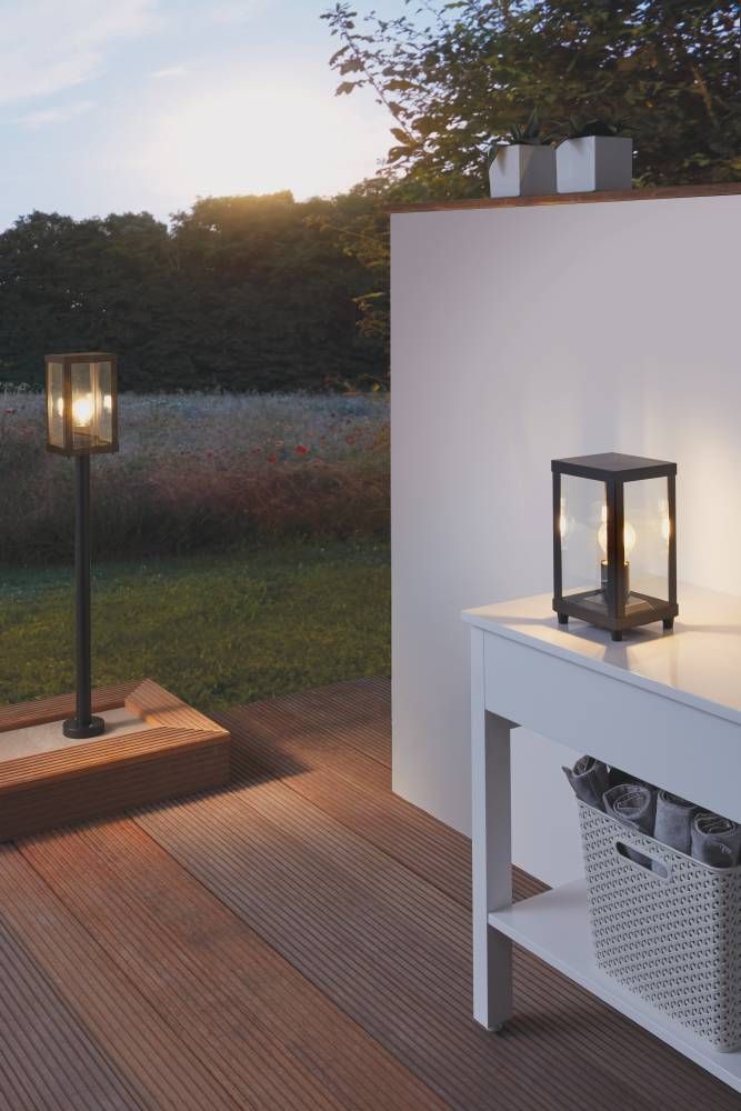 Lampadaire sur terrasse en bois avec lanterne posée sur table, au coucher du soleil.