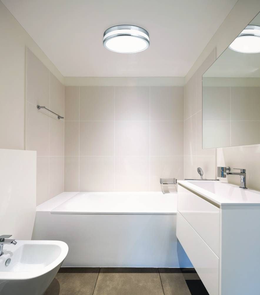 Vue en situation dans une salle de bain blanche, plafonnier allumé au-dessus de la baignoire