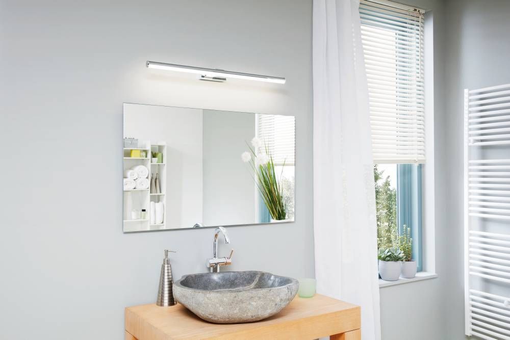Mise en ambiance salle de bain, applique fine allumée au-dessus d'un miroir rectangulaire.