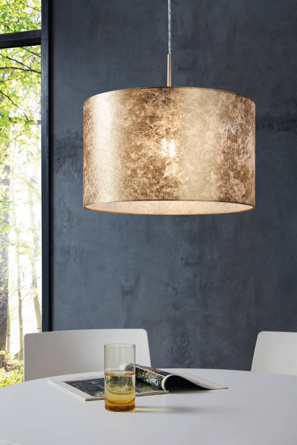 Vue rapprochée du luminaire suspendu éclairant une table avec verre et magazine.