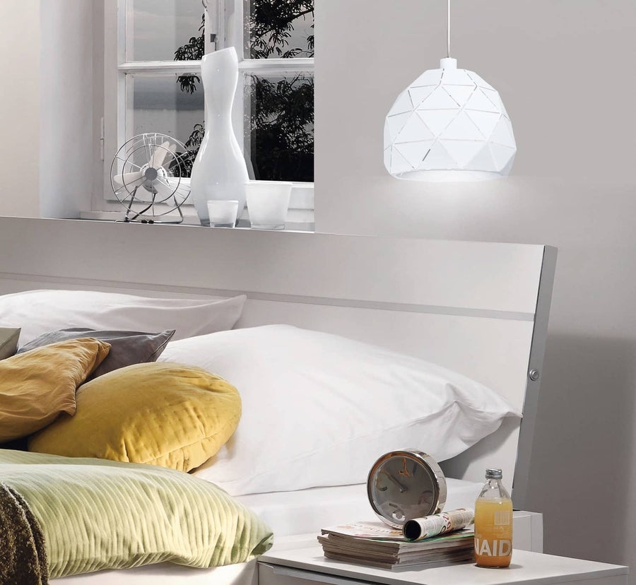 Suspension blanche allumée dans une chambre, au-dessus d'un lit avec coussins jaunes.