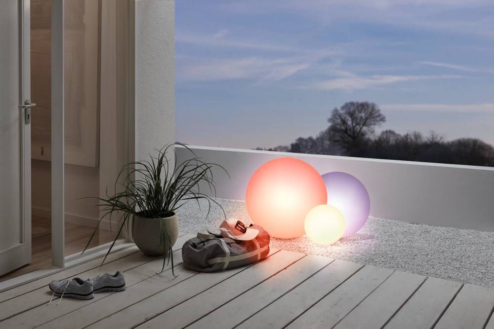 Mise en ambiance sur terrasse, trois sphères lumineuses colorées près d'une plante et d'un sac