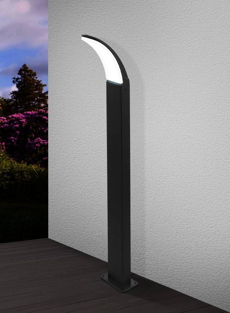 Lampadaire installé sur terrasse en bois devant mur crépis, jardin fleuri en arrière-plan