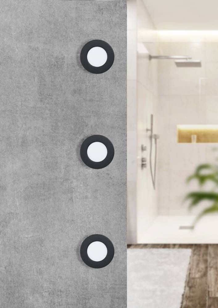Trois spots encastrés noirs et blancs alignés verticalement sur un mur gris de salle de bain.