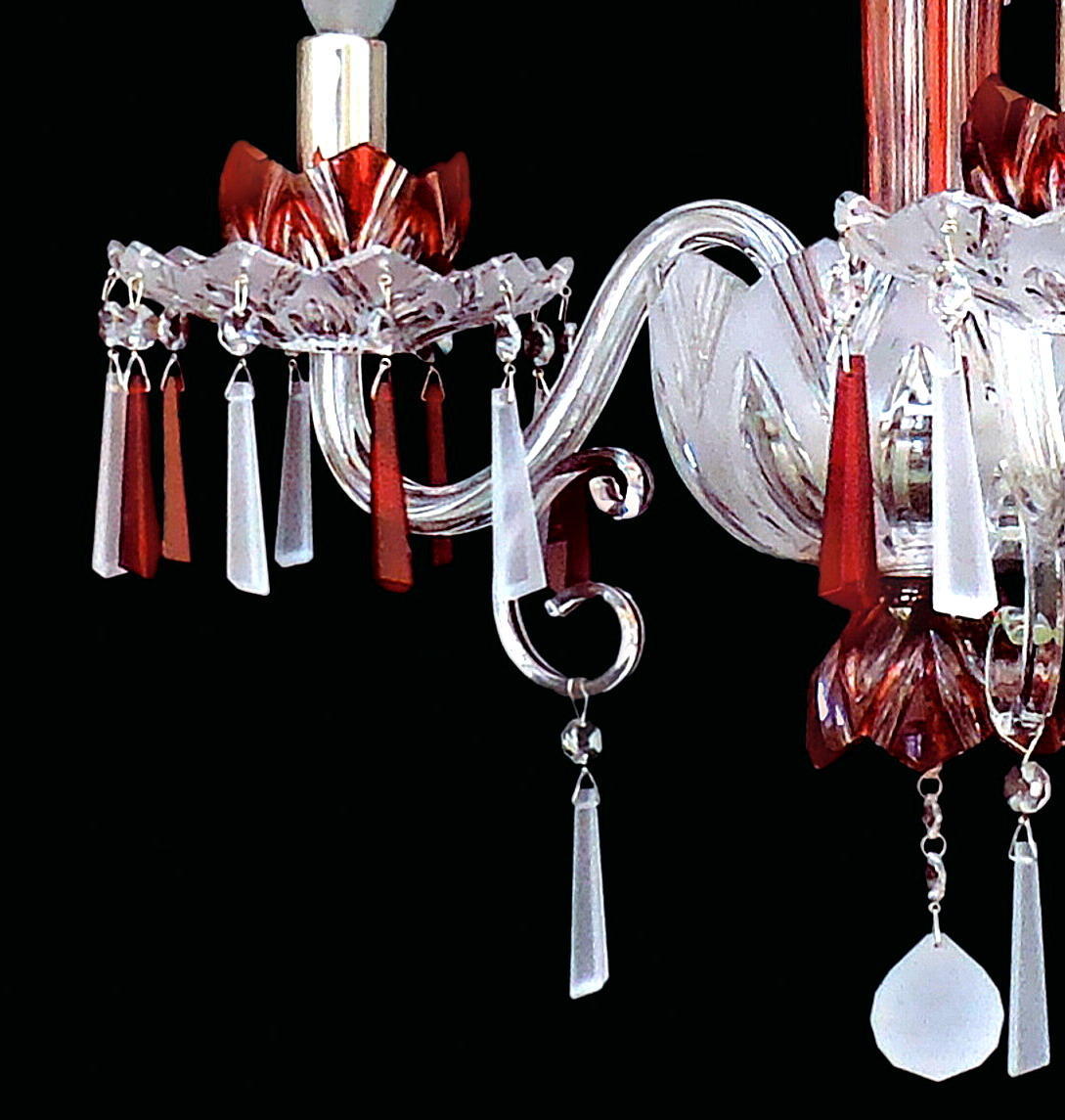 Détail d'un bras courbé en verre transparent avec bobèche, fleurs rouges et pendants rectangulaires.