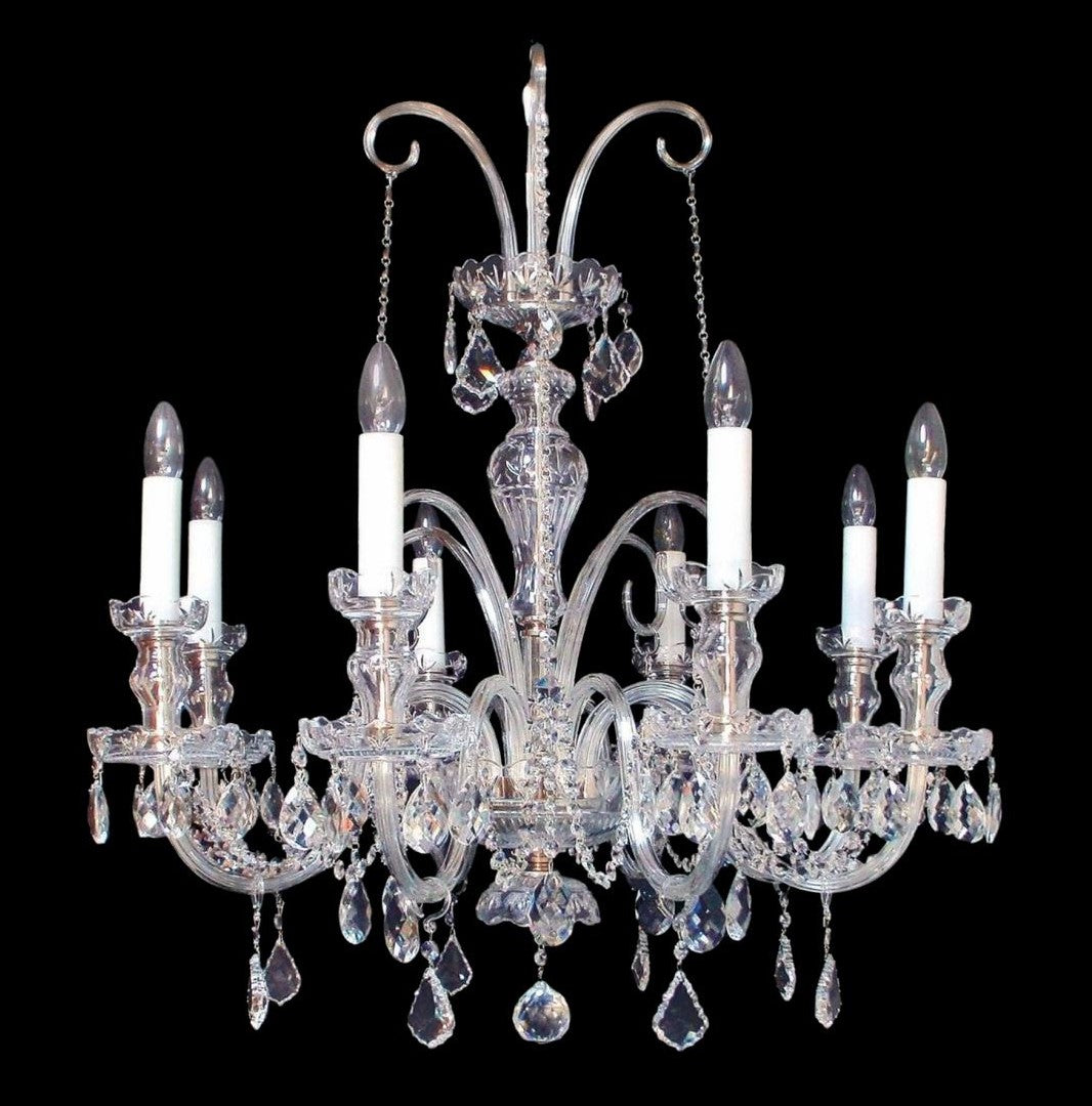 Lustre en cristal à bras courbés, bougies blanches et pendeloques, vu de face sur fond noir.