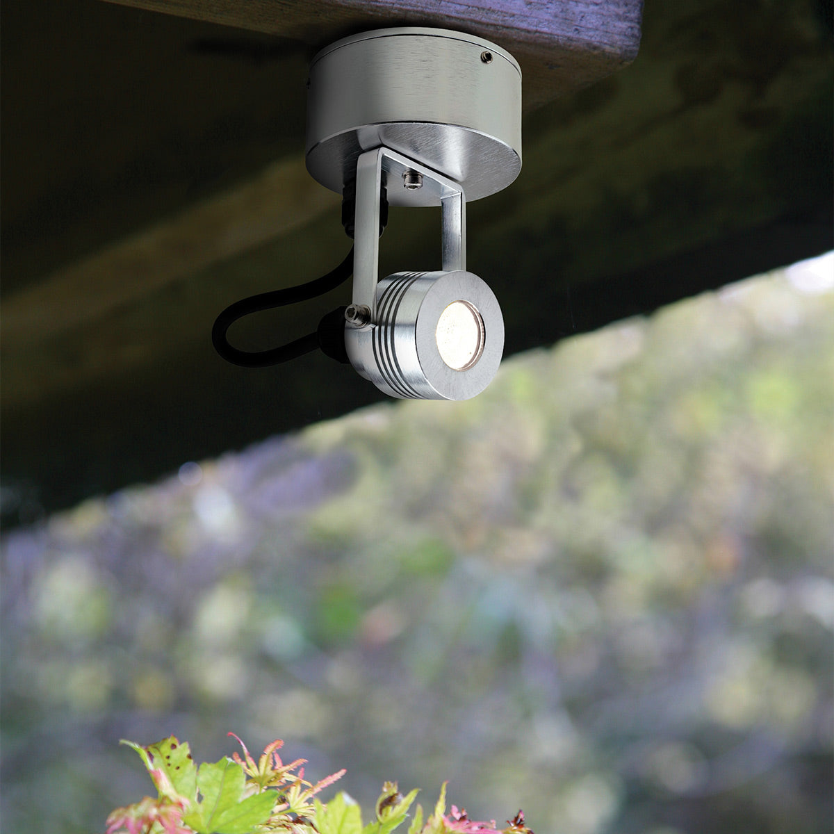 Spot en aluminium fixé sous une poutre en bois, orienté vers le bas dans un jardin