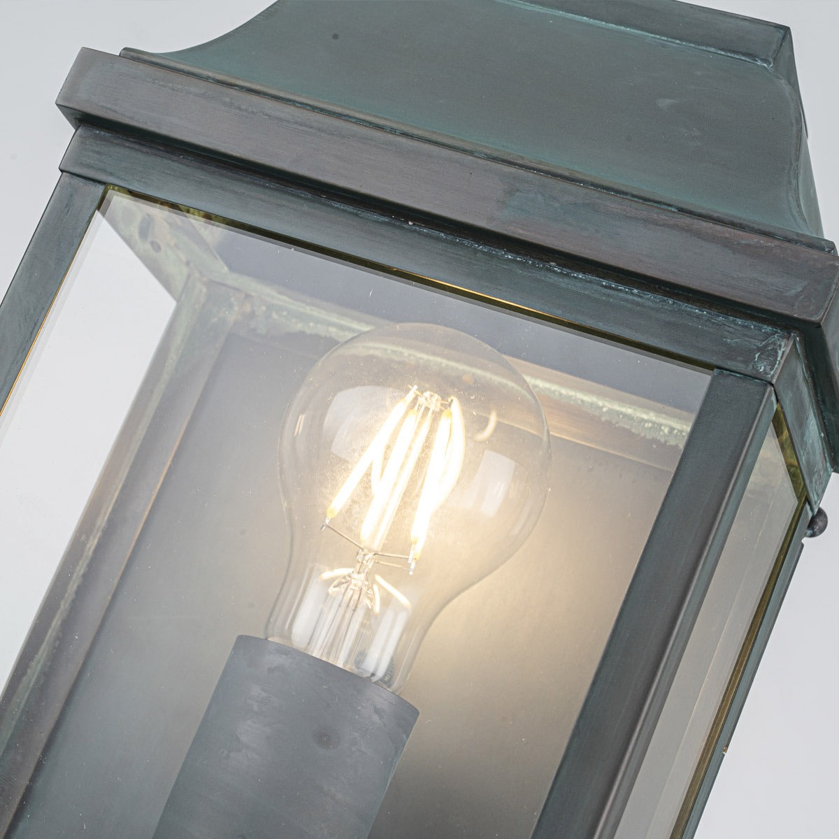 Détail du haut du luminaire avec verre biseauté et ampoule ronde allumée