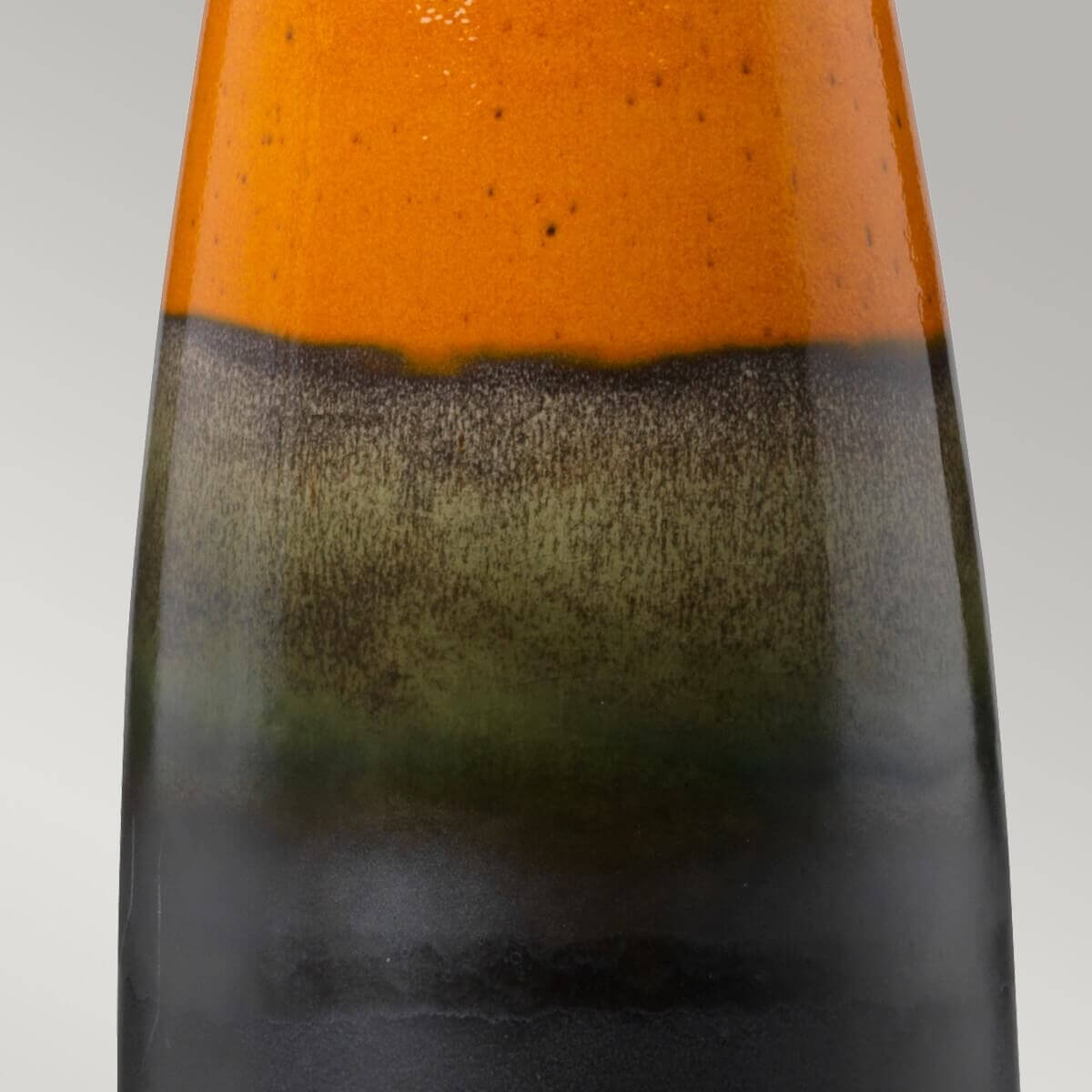 Gros plan sur la transition glaçure entre orange moucheté et noir fondu du pied céramique.