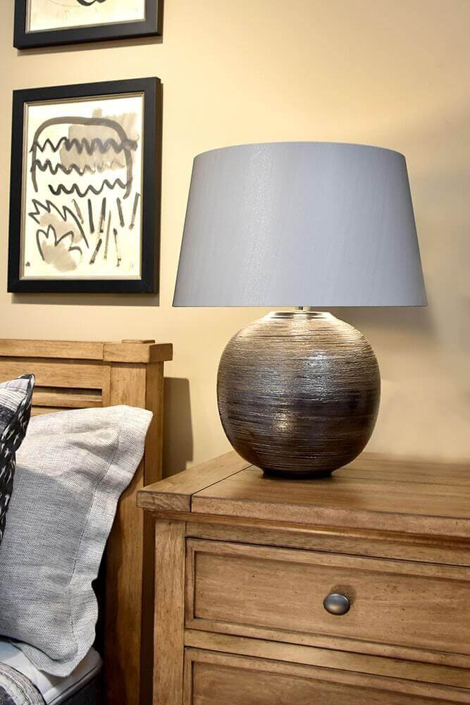 Lampe posée sur une table de chevet en bois, cadres noirs au mur
