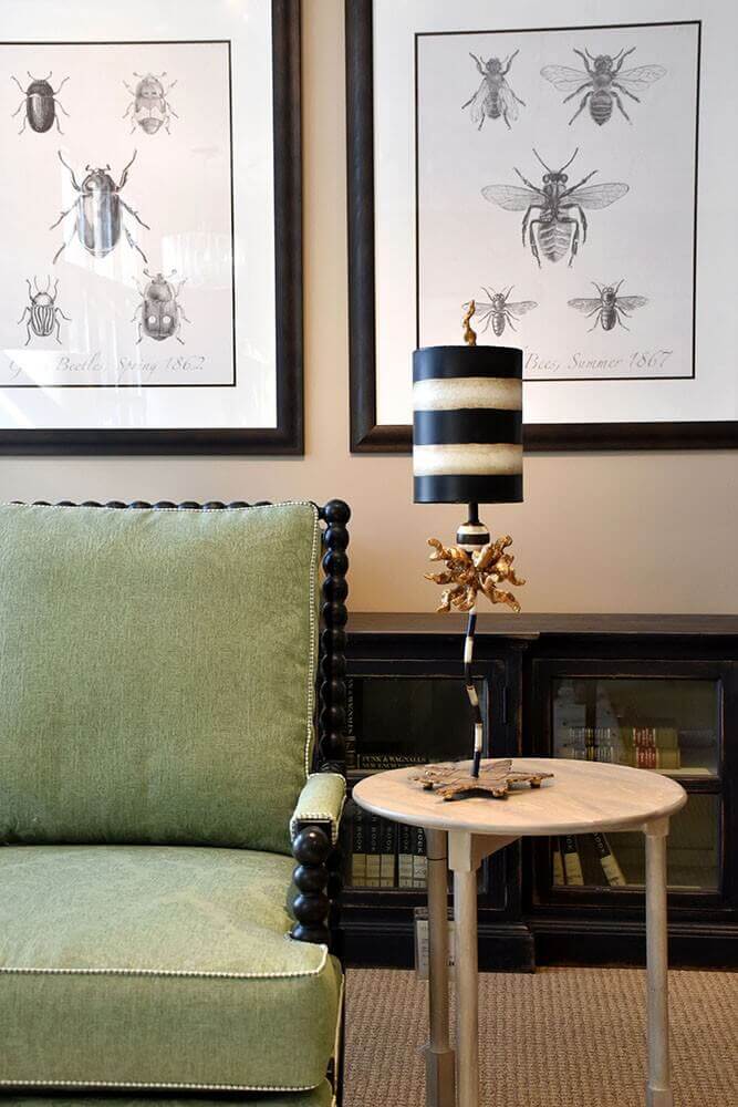 Mise en ambiance salon avec fauteuil vert, affiches entomologiques et lampe posée sur table basse