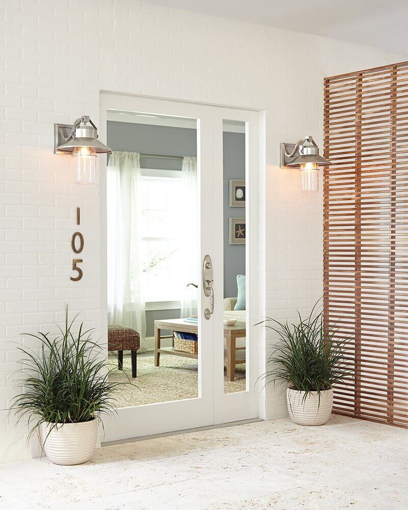 Deux appliques encadrant une porte-miroir sur façade de briques, plantes en pots