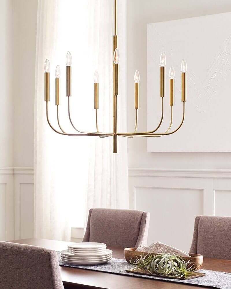 Vue en ambiance du lustre allumé au-dessus d'une table dressée, dans une pièce claire.