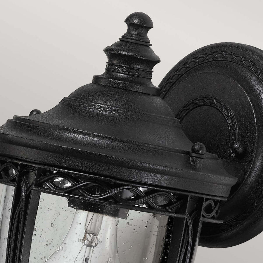 Détail du chapeau sommital noir et de la platine murale ronde ornée.