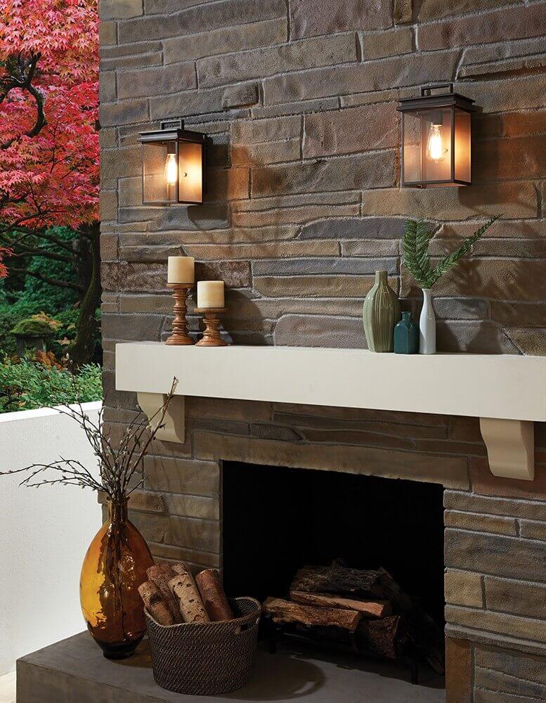 Mise en ambiance sur mur de pierre avec cheminée, deux appliques allumées et décor automnal.