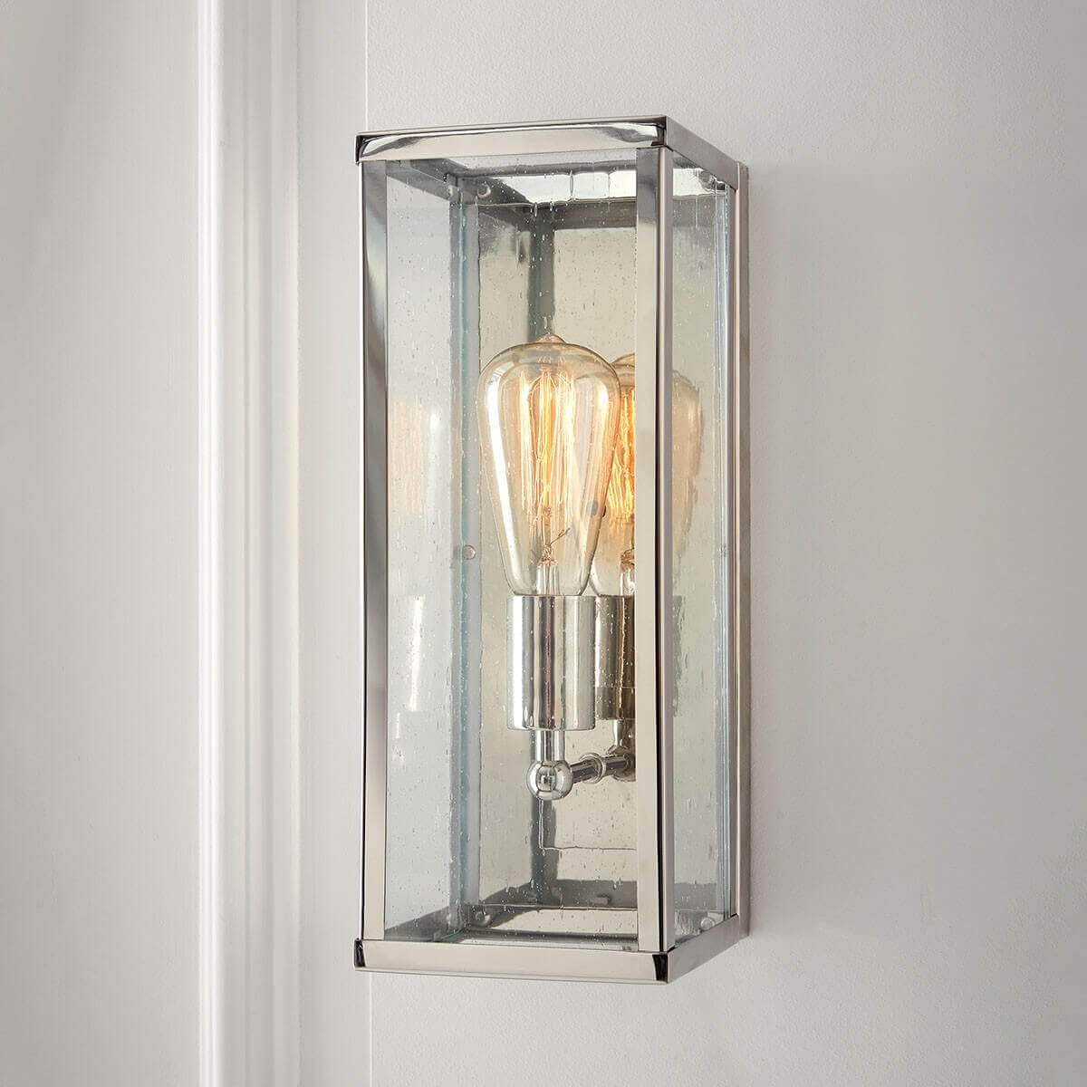 Applique fixée sur mur blanc, ampoule Edison allumée derrière le verre moucheté