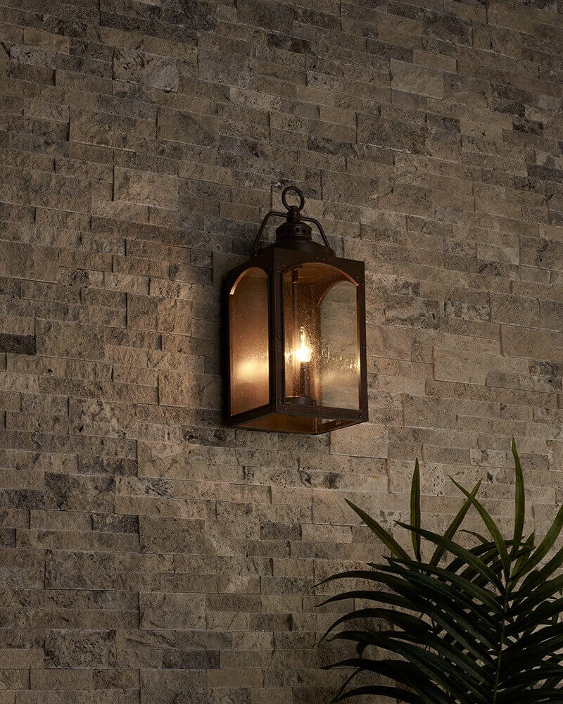 Mise en ambiance nocturne sur mur en pierre, applique allumée et feuillage