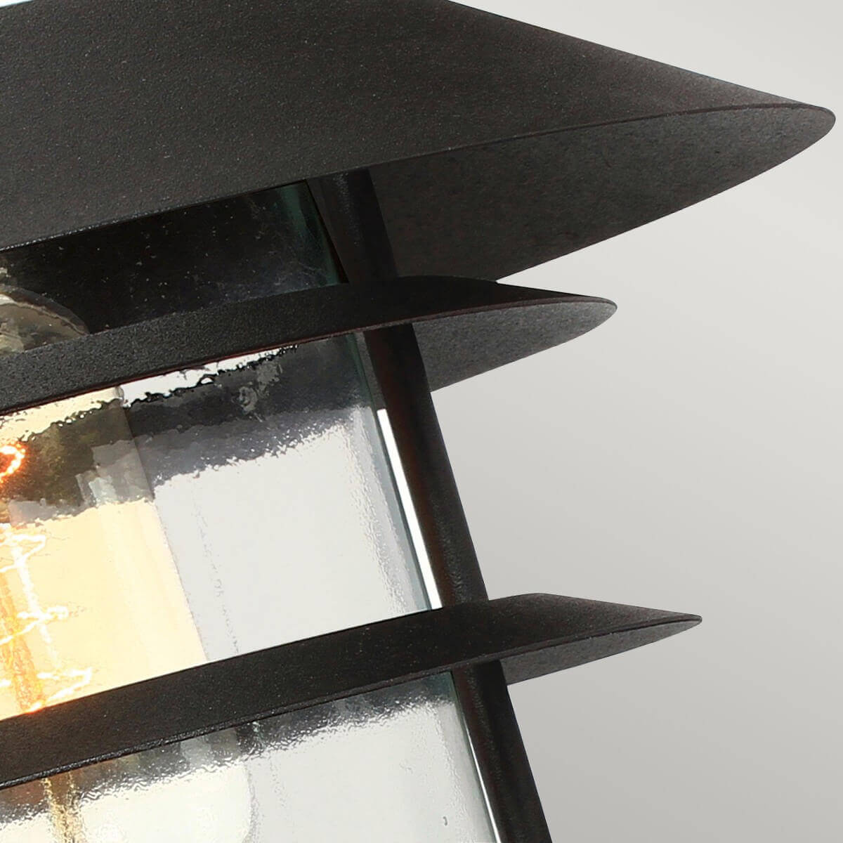 Détail des ailettes métalliques noires entourant le verre transparent du luminaire