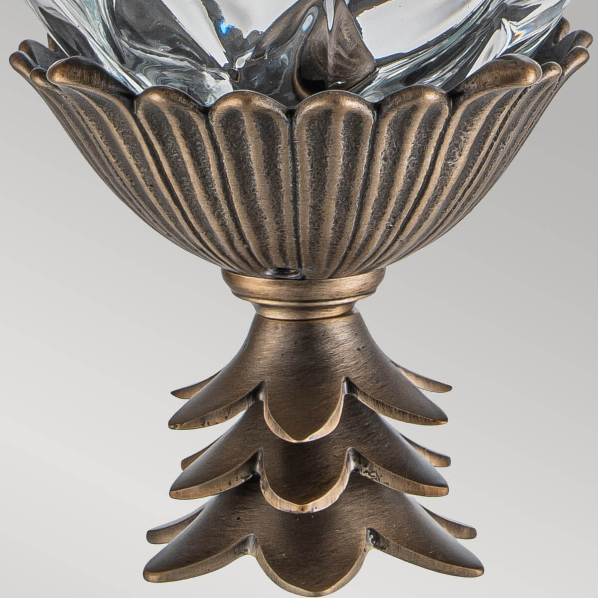Gros plan du culot inférieur godronné et des feuilles de bronze patiné sous le verre