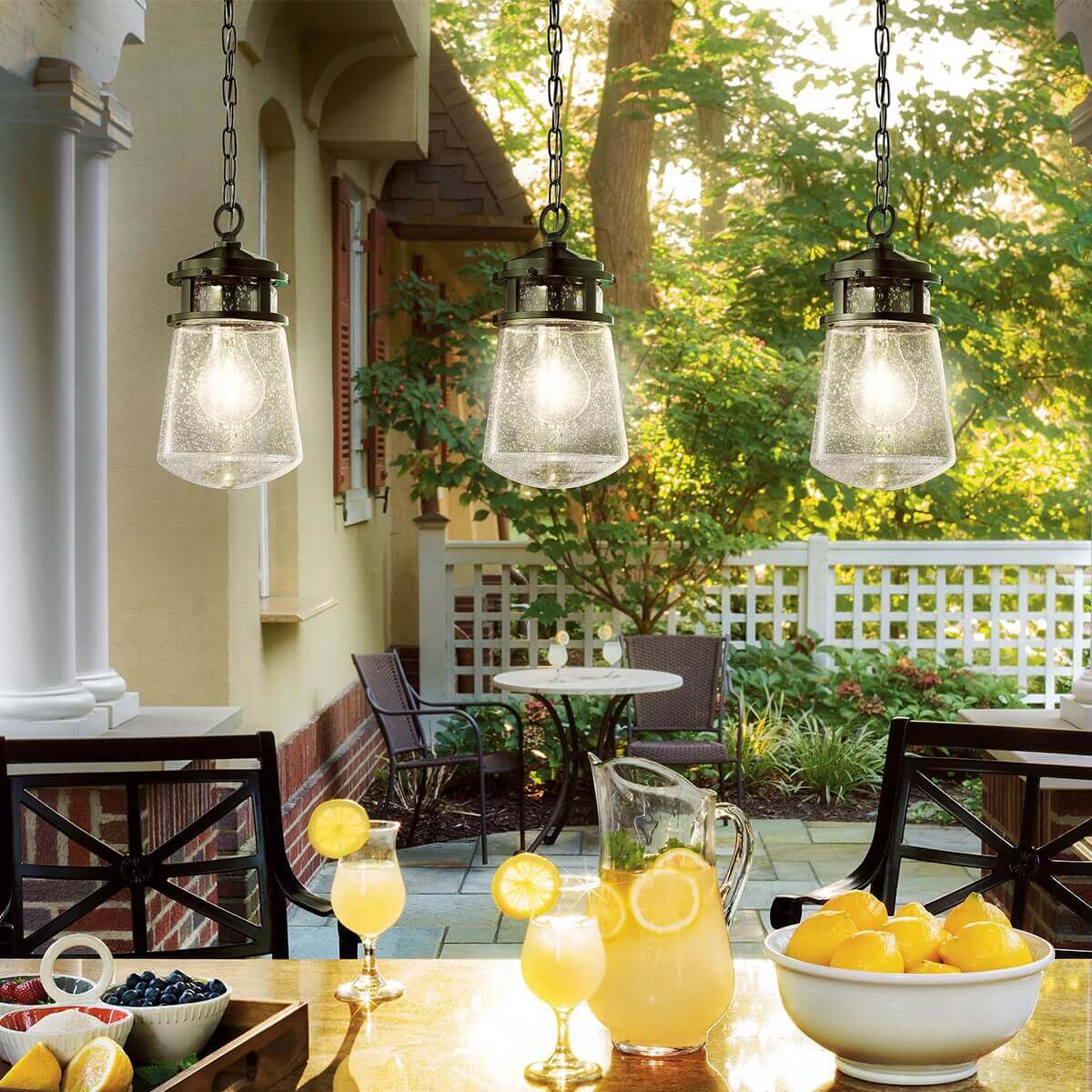Mise en ambiance extérieure avec trois suspensions allumées au-dessus d'une table de jardin.
