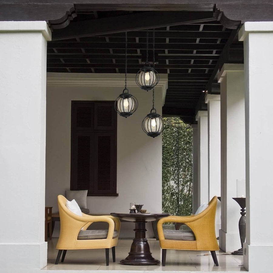 Trois suspensions noires suspendues sous une pergola, au-dessus d'un coin salon extérieur.
