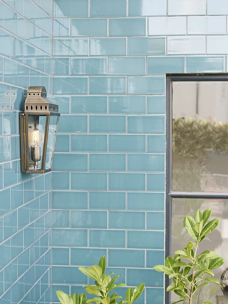 Vue en situation de l'applique fixée sur un mur carrelé bleu, près d'une fenêtre