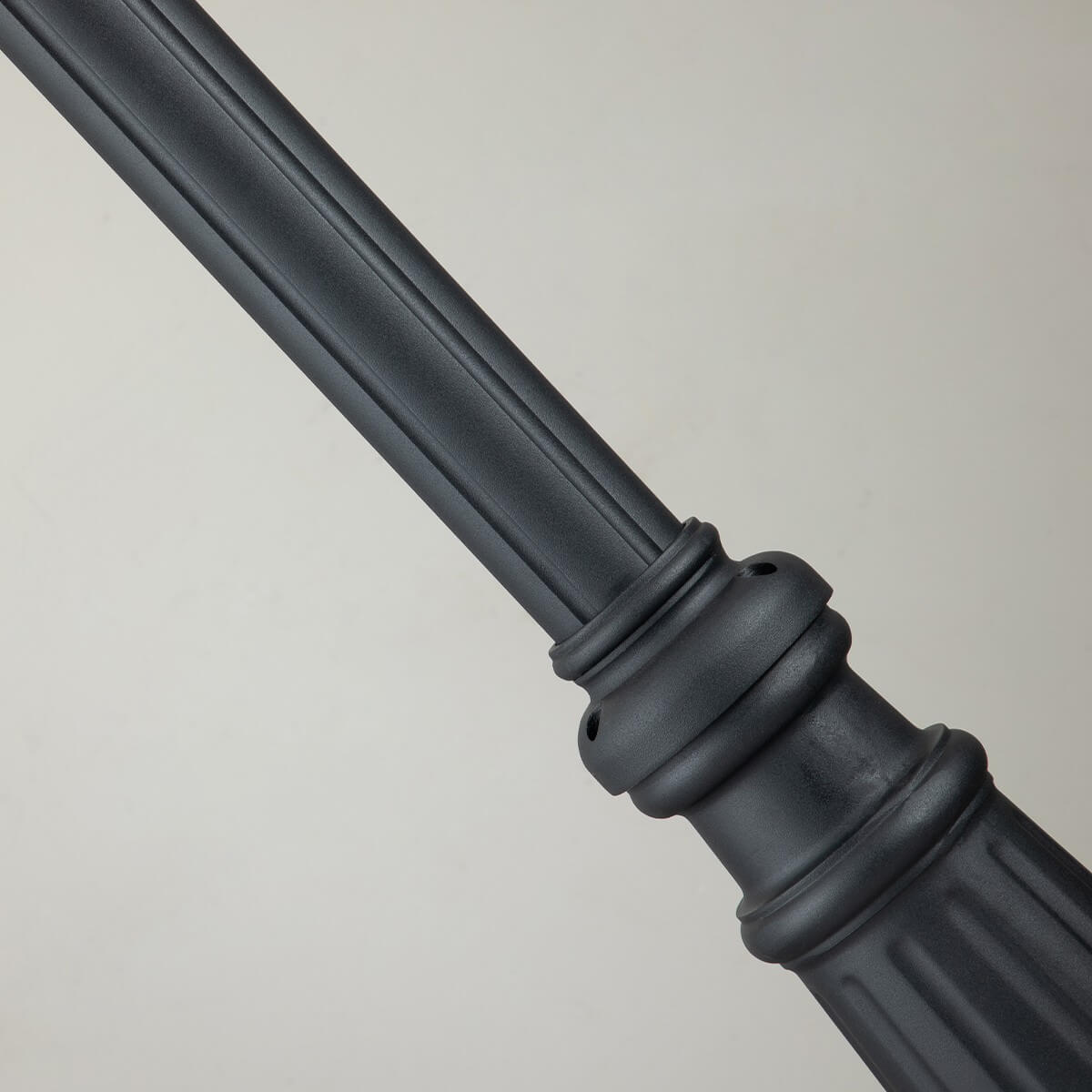 Détail du fût et de la base moulurée noire avec rainures verticales et bagues décoratives.
