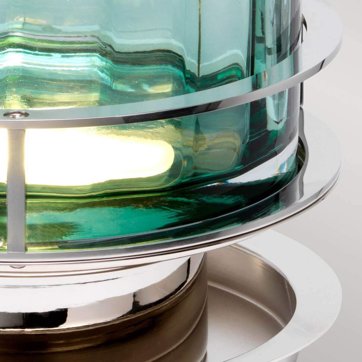 Détail du bas de la lampe, verre vert rétroéclairé et socle métallique brillant.
