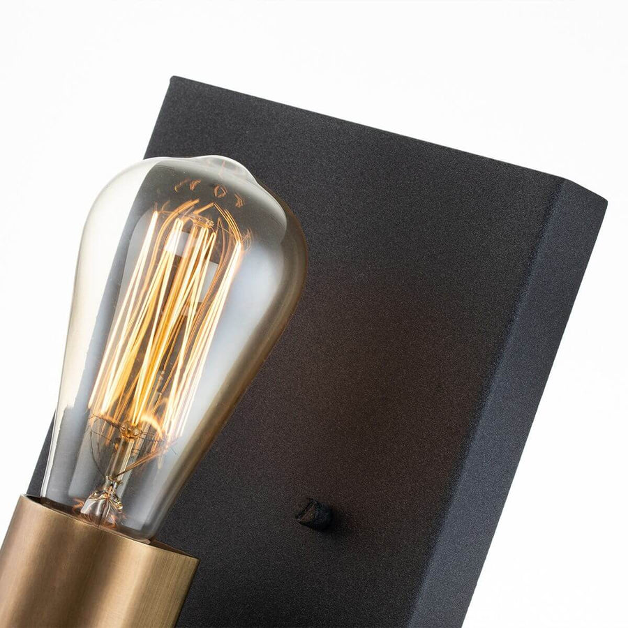 Détail de l'ampoule Edison allumée devant la platine murale noire texturée