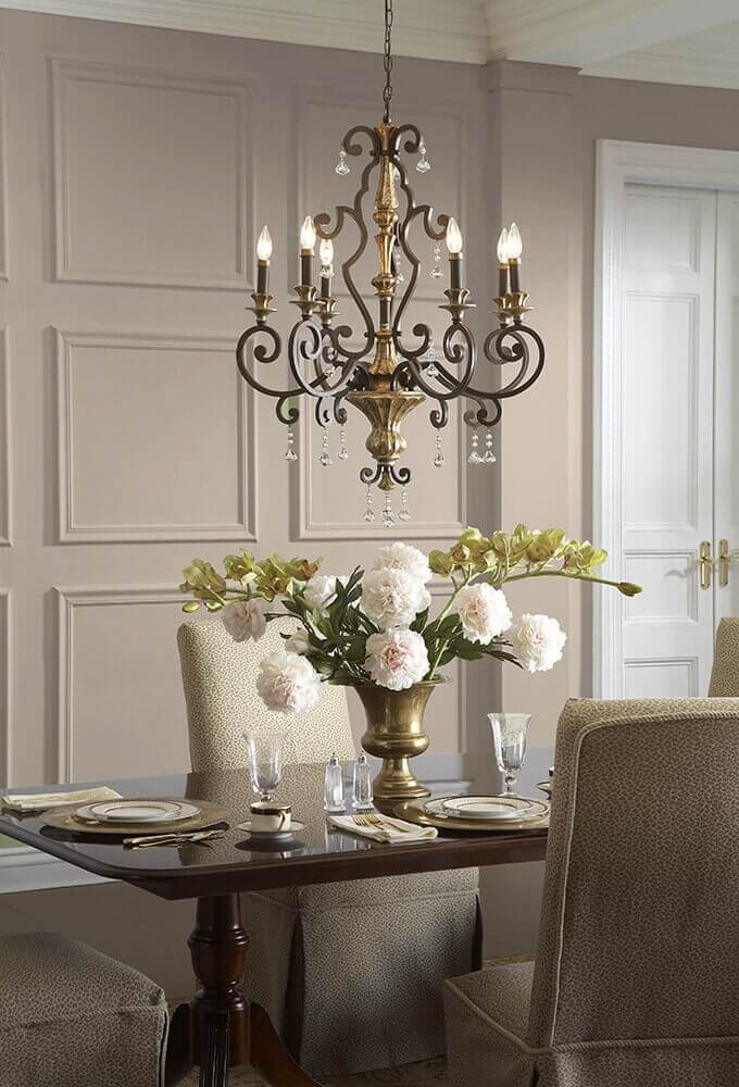 Lustre allumé au-dessus d'une table dressée avec fleurs, mur lambrissé gris clair.