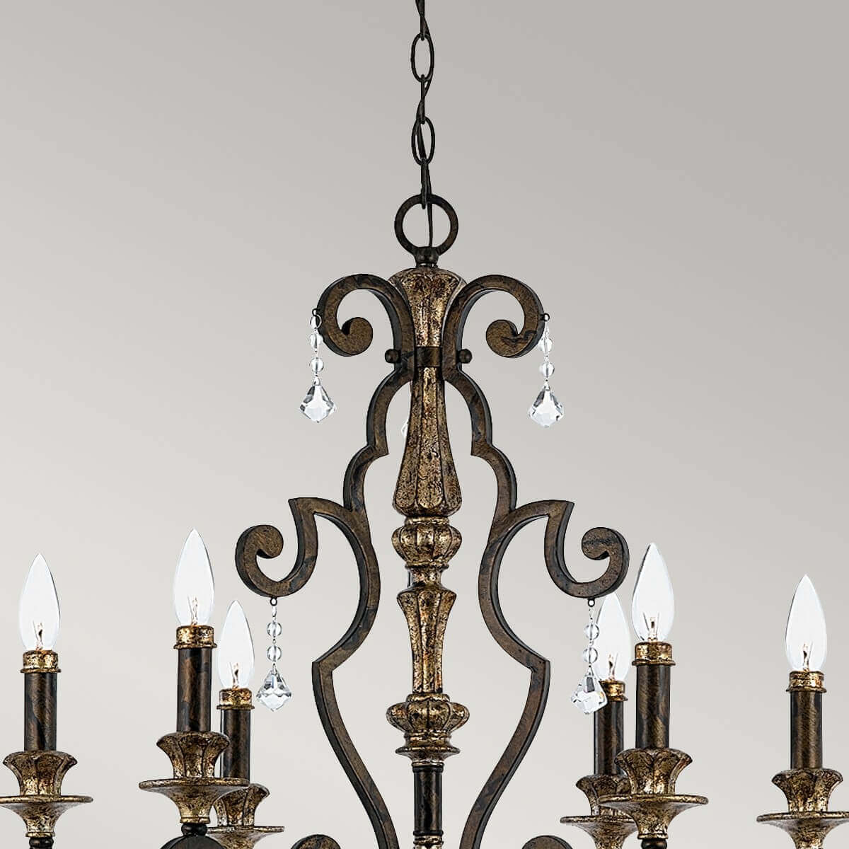 Détail du haut du lustre : chaîne, volutes métalliques et pendentifs en cristal.
