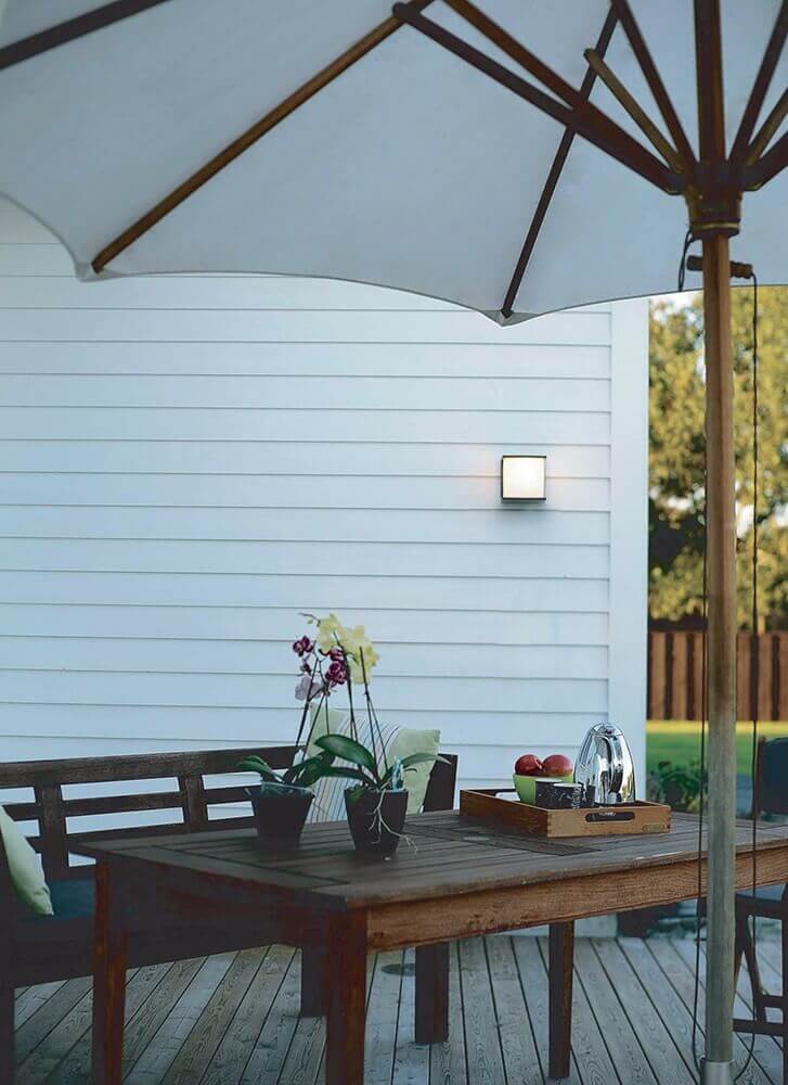 Mise en ambiance sur terrasse, table en bois, parasol et applique éclairée