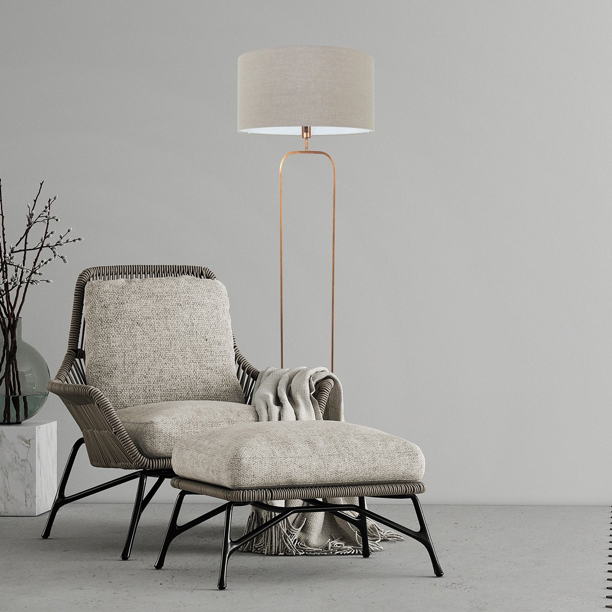 Mise en ambiance salon avec fauteuil tissu, plaid et lampadaire allumé contre mur gris.