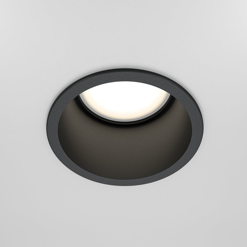 Spot encastré noir rond vu de face dans un plafond blanc