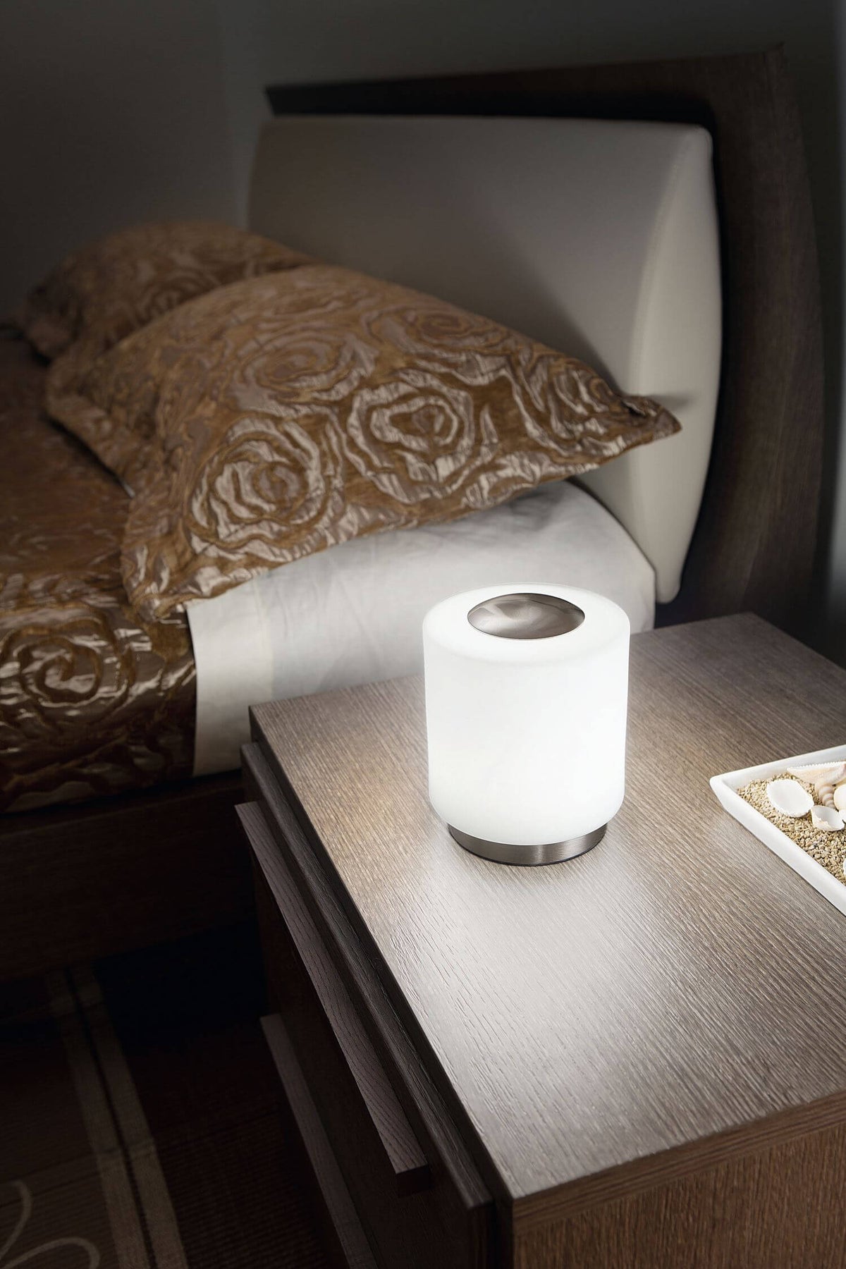 Lampe posée sur table de chevet en bois, près d'un lit, ambiance chambre tamisée