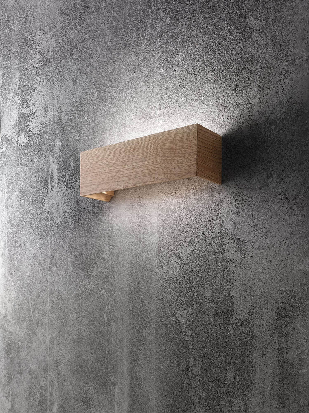 Même applique en bois installée sur un mur béton brut, lumière diffusée vers le bas