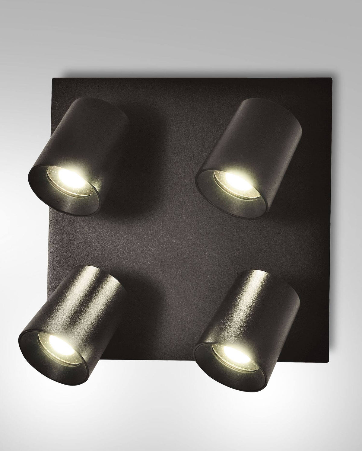 Vue de face du spot noir à quatre lumières orientables allumées sur fond blanc