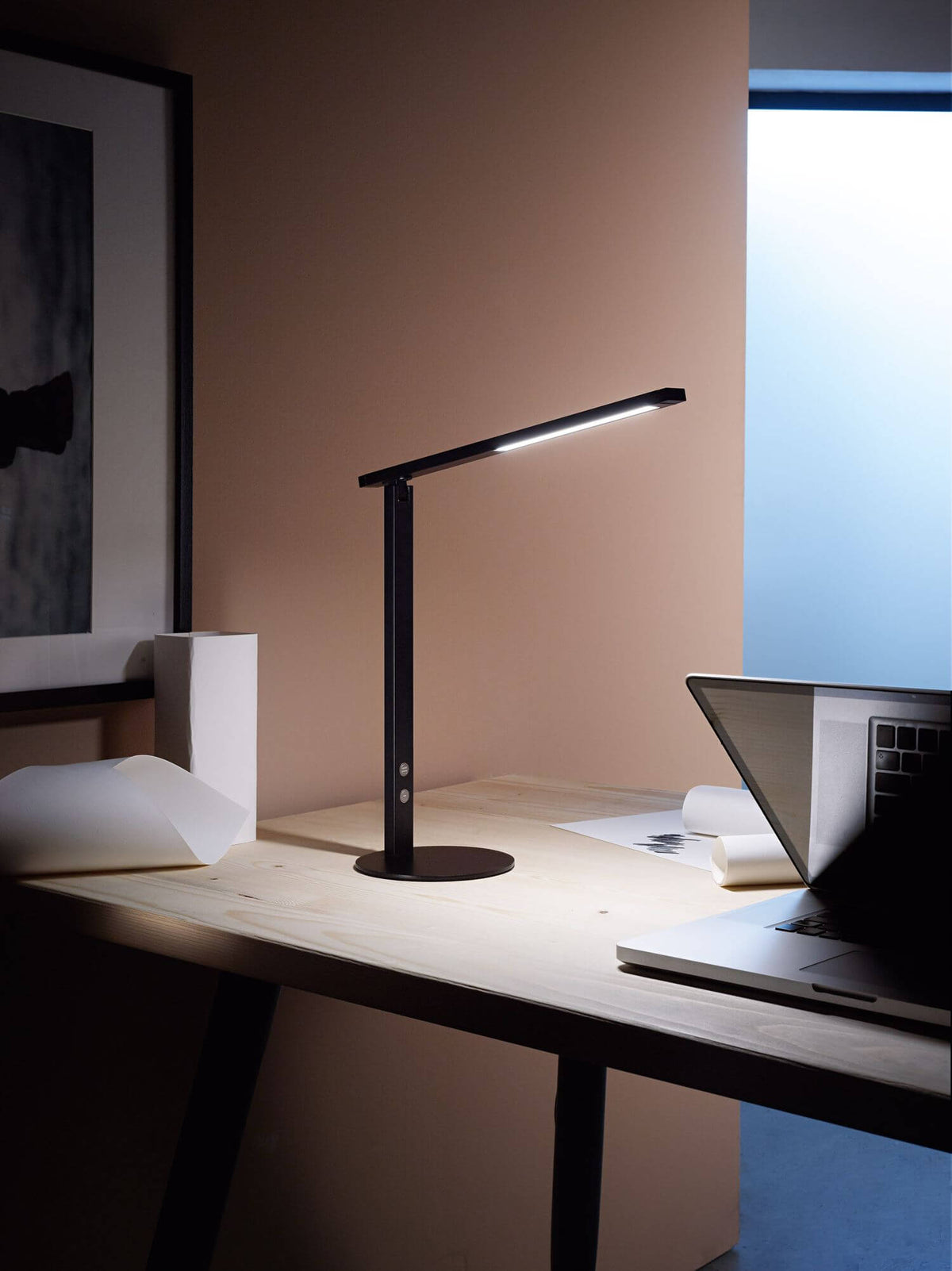 Mise en ambiance sur un bureau en bois clair, près d'un ordinateur portable et de documents.