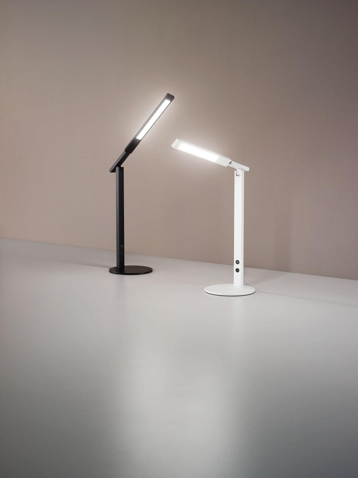 Deux lampes de bureau identiques, blanche et noire, posées côte à côte en ambiance