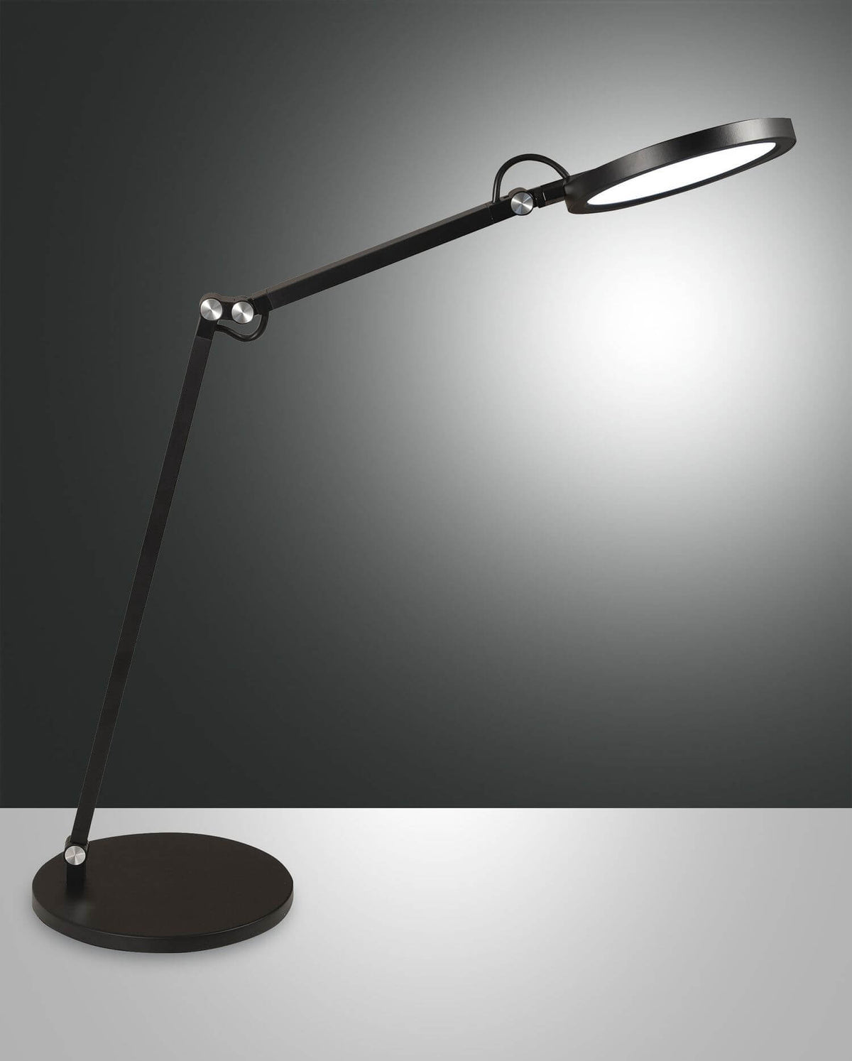 Lampe à poser noire articulée, tête ronde et base plate, sur fond gris dégradé.