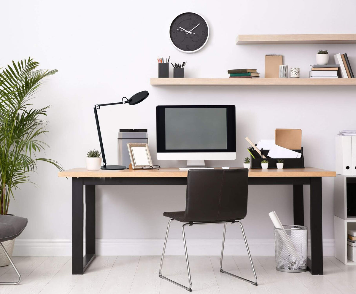 Lampe à poser noire installée sur un bureau en bois dans un intérieur lumineux.