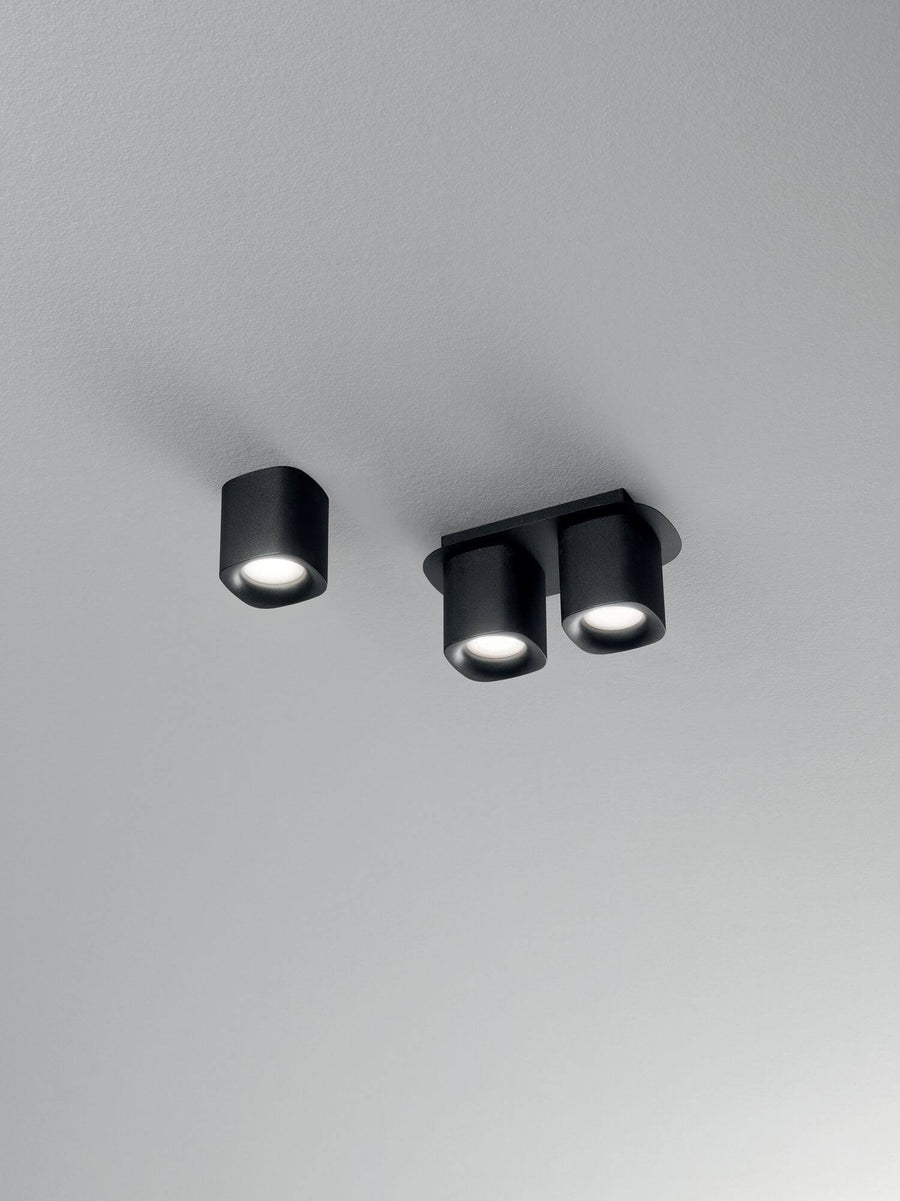 Vue de dessous sur plafond gris, un spot simple et un spot double noirs allumés.